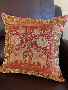 an orange and gold decorative pillow on a brown leather couch with a black chair in the background