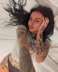 a woman laying in bed with tattoos on her arms and legs, covering her face