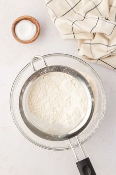 a whisk in a glass bowl next to a wooden spoon on a white surface