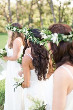 bridesmaids in white dresses with greenery wreaths on their heads looking at each other