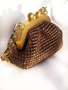 a brown purse with gold chain and two balls on the clasp, sitting on a white surface