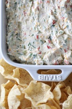 a white bowl filled with dip surrounded by tortilla chips