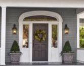 a gray house with white trim and two front porches on the first floor, surrounded by greenery