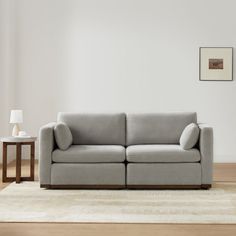 a gray couch sitting on top of a wooden floor next to a white table and lamp