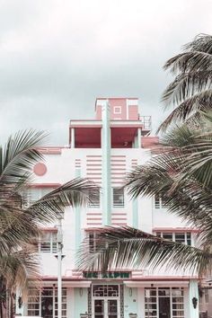 a pink and white building with palm trees in front of it on a cloudy day