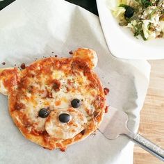 a pizza with cheese and black olives on it next to a bowl of salad