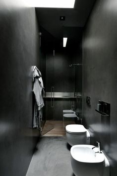 two white toilets sitting next to each other in a black and white bathroom with skylights