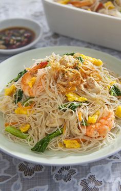 a white plate topped with noodles and vegetables next to a bowl of soup on a table