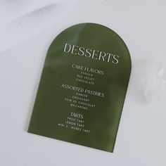 a green sign that says desserts on the front and back of it, sitting on top of a white table