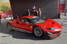 a red sports car parked in front of a black wall with people standing around it