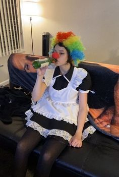 a woman sitting on a couch with a clown wig drinking from a bottle in her hand