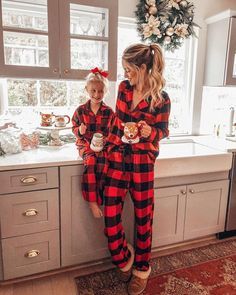 two girls in matching pajamas standing on the kitchen counter and looking at each other while holding coffee mugs