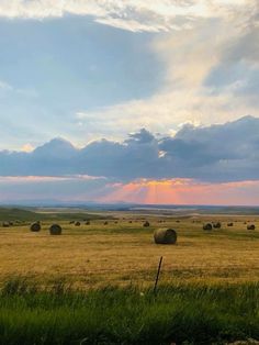 the sun is setting over a field full of hay bales