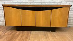 a wooden cabinet sitting on top of a hard wood floor next to a brick wall