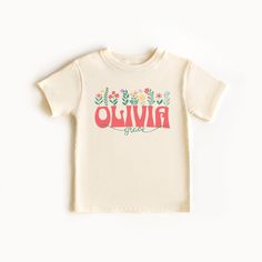 Let the sweet toddler girl in your life show off her beautiful name with this personalized floral t-shirt. Groovy retro lettering and a swirly script font are paired with colorful pastel flowers on this super soft tee. The shirt can be customized with a child's first and middle name; if you would like only the first name, just let us know in the personalization section. This pretty graphic tee would make a great gift for any little girl this holiday season, and it comes in toddler sizes 2T - 5T. Custom Name Short Sleeve T-shirt For Birthday, Personalized Pink T-shirt For Summer, Personalized Cotton T-shirt With Letter Print, Personalized Short Sleeve T-shirt For Spring, Custom Name Cotton T-shirt With Short Sleeves, Personalized Pink Tops For Spring, Personalized Cotton Short Sleeve T-shirt, Personalized Name Print Short Sleeve Tops, Personalized Pink Top For Spring