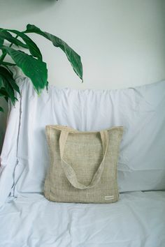 a bag sitting on top of a white bed next to a green leafy plant