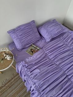 a bed with purple sheets and pillows on top of it next to a small table