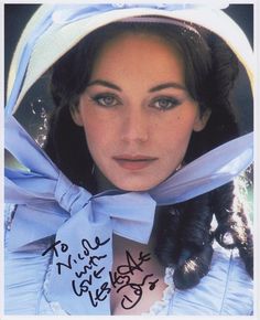 a woman wearing a white hat and blue dress with a ribbon around her neck is looking at the camera