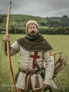 a man dressed in medieval clothing holding a bow and arrow while standing on a field