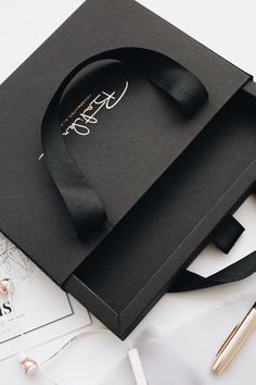 an open box with a black ribbon on top of it and a pen next to it