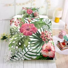 a bed covered in pink and green flowers on top of a wooden floor next to a white wall