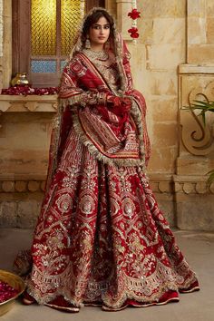 a woman in a red and gold bridal gown standing next to a bowl of rose petals