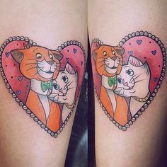 two cats in a heart shaped frame tattoo on both thighs, one with an orange cat and the other has a green bow tie