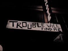 a sign that says trouble will find me on the side of a building at night