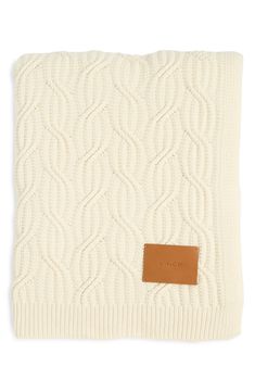 a white knitted blanket with a brown leather tag on the front and back of it