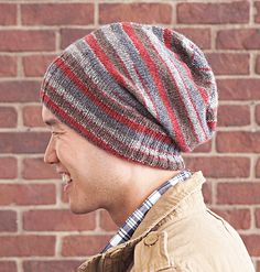 a man wearing a striped hat standing in front of a brick wall with his head turned to the side