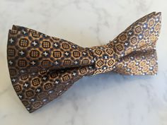 Upgrade your wardrobe in style with this stunning bronze mosaic pattern bow tie. Perfect gift for him, this unique adjustable bow tie will elevate your style for any occasion including weddings, birthdays and anniversaries. Comes pre-tied. Adjustable Gold Bow Tie, Brown Bow Tie For Party, Adjustable Brown Bow Tie For Party, Gift Gold Bow Tie, Brown Satin Bow Tie For Party, Elegant Brown Bow For Party, Dapper Brown Bow Tie For Party, Brown Dapper Bow Tie For Party, Floral Bow Tie