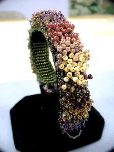 a close up of a bracelet on a black stand with beads and flowers in it