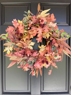 a wreath is hanging on the front door with autumn leaves and other foliage around it