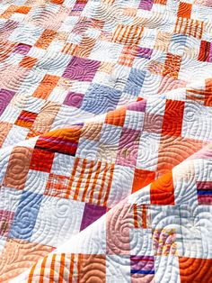 an orange and white quilt is laying on top of a tablecloth that has squares in it