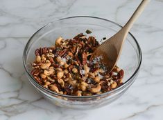 a glass bowl filled with nuts on top of a marble countertop next to a wooden spoon