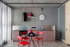 a dining room table with red chairs and a black counter top in front of a gray wall