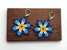 two blue and yellow beaded earrings sitting on top of a wooden board next to each other