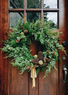 a wreath on the front door of a house with pine cones and greenery hanging from it