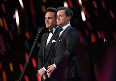 two men in tuxedos standing next to each other at a microphone on stage