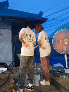 two people standing next to each other in front of a blue tarp