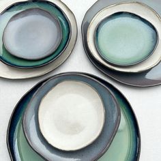 three plates with green and blue designs on them sitting on a white tableclothed surface