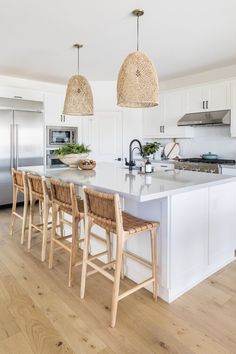 a kitchen with white cabinets and wooden chairs in front of an island that has two pendant lights above it