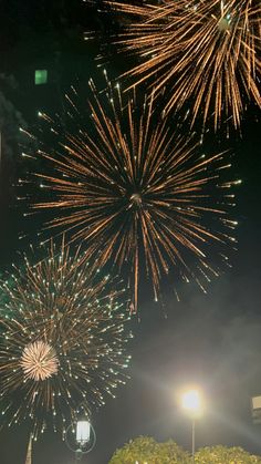 fireworks are lit up in the night sky above trees and street lights on a city street