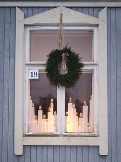 a wreath is hanging on the window sill in front of candles that are lit