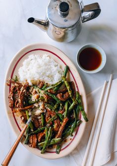 a plate with rice, meat and green beans next to a teapot on a table