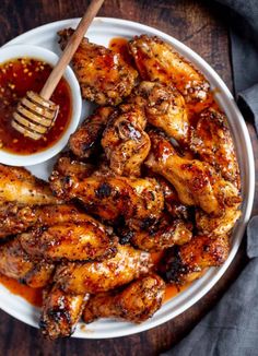 a white plate topped with chicken wings next to a small bowl of bbq sauce