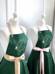 two mannequins dressed in green aprons with pink sashes on them