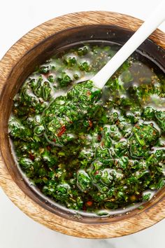 a wooden bowl filled with broccoli soup and a white spoon in the middle