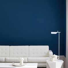 a white couch sitting in front of a blue wall next to a table with a lamp on it