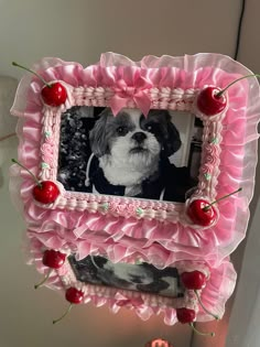 a pink frame with a dog and cherries hanging from it's sides, in front of a wall